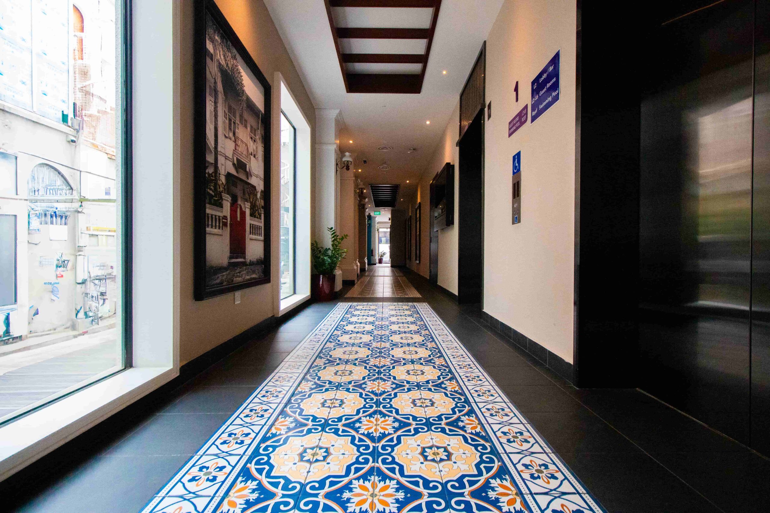 Walkway and lift lobby showing off peranakan floor tiles and portraits of heritage buildings.